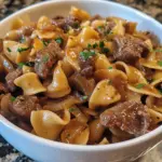 Crock pot French onion beef and noodles served in a bowl with fresh herbs