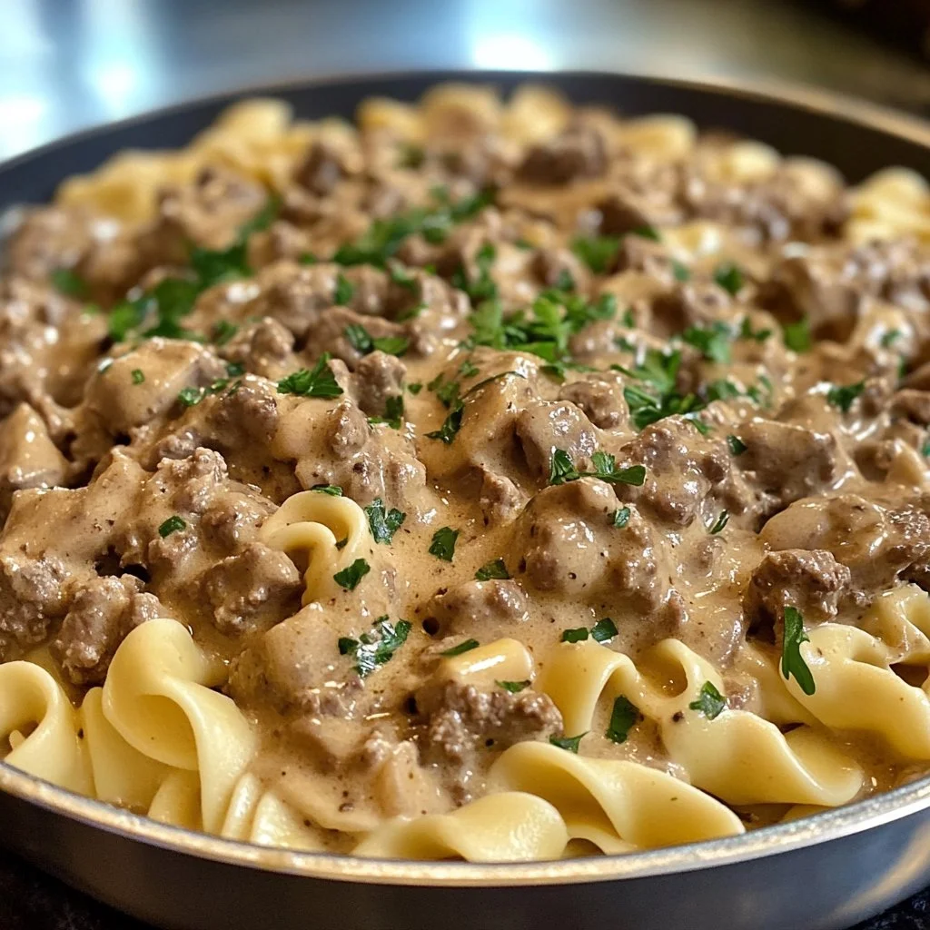 Creamy ground beef stroganoff served over noodles with fresh herbs