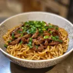 A delicious plate of Hoisin Beef Noodles garnished with vegetables and herbs.