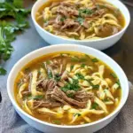 Slow cooker beef noodles in a bowl with fresh herbs garnish.
