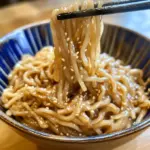 Plate of soy sauce noodles topped with vegetables and sesame seeds