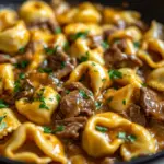 Cheesesteak tortellini served in a creamy provolone sauce, garnished with herbs.
