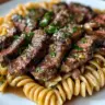 Plate of Garlic Butter Steak served with pasta, garnished with herbs.