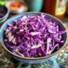 Colorful red cabbage slaw served in a bowl with fresh vegetables.