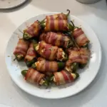 Bacon wrapped jalapeno poppers served on a plate, garnished with fresh herbs.