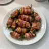 Bacon wrapped jalapeno poppers served on a plate, garnished with fresh herbs.