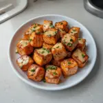 Bang Bang Salmon Bites served on a plate with spicy sauce and garnish.