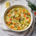 Bowl of cozy Greek lemon chicken soup with fresh herbs and lemon slices