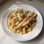 Creamy pasta dish with sweet peas and crispy pancetta garnished on a plate.