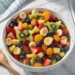 Delicious fruit salad drizzled with honey lime dressing, served in a bowl.