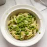 Bowl of pasta with peas and parmesan cheese garnished with fresh herbs.