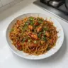 Plate of sticky garlic chicken noodles garnished with herbs