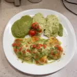 Creamy pesto baked chicken garnished with fresh herbs on a white plate