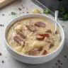 Bowl of creamy sausage, potato, and sauerkraut soup topped with fresh herbs