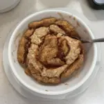 Easy cinnamon roll baked oatmeal in a dish, topped with icing and cinnamon.