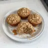 Moist applesauce oatmeal muffins served on a plate, topped with oats.