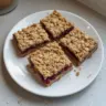 Homemade oatmeal bars on a wooden table with ingredients in the background.