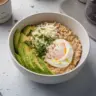 Bowl of savory avocado oatmeal topped with fresh herbs and spices