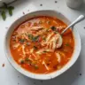 Bowl of spicy chicken soup garnished with herbs and spices