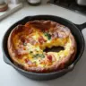 Delicious Cheddar Bacon Dutch Baby served on a plate with fresh herbs.