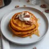 Fluffy sweet potato pancakes stacked on a plate with syrup and butter