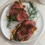 Marinated venison backstrap served on a plate with herbs and spices