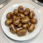 Plate of grilled baby new potatoes garnished with herbs and spices.