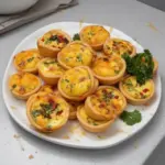A platter of assorted mini quiches filled with vegetables and cheese.