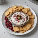 Cranberry Jalapeño Dip served in a bowl with crackers and fresh herbs