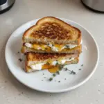 Goat cheese grilled cheese sandwich drizzled with honey on a wooden board.