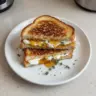 Goat cheese grilled cheese sandwich drizzled with honey on a wooden board.