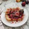 Jar of homemade fig jam with fresh figs and bread on a wooden table