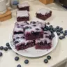 Glazed blueberry brownies topped with a sweet glaze on a rustic table.