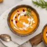 Bowl of homemade carrot sweet potato soup topped with herbs.