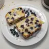 Iced Lemon Blueberry Loaf with icing and fresh blueberries on a white plate